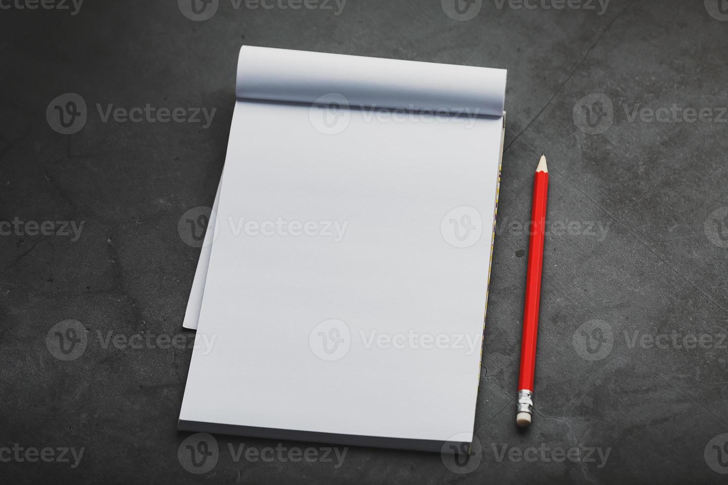 cahier avec un crayon rouge sur fond sombre pour l'écriture. espace vide libre pour écrire sur une feuille vierge d'un cahier, photo