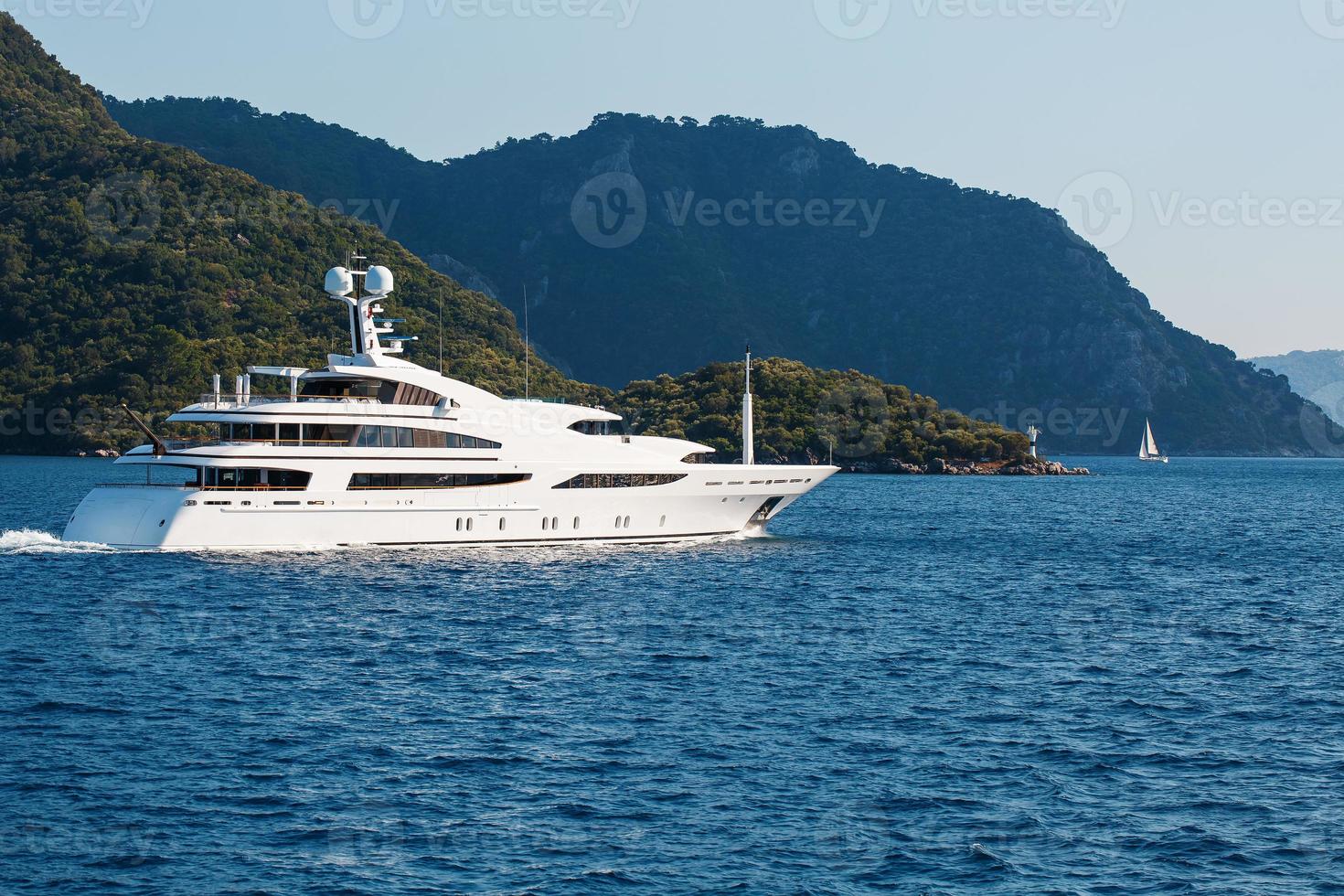 beau yacht blanc moderne avec voile sur la mer bleue, sur fond de montagnes. photo