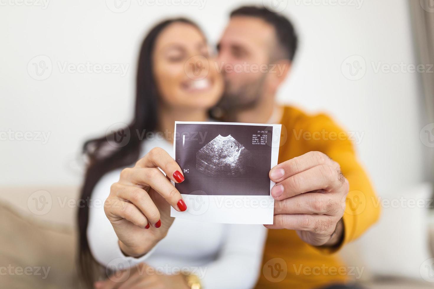 femme enceinte heureuse avec photo échographique de bébé embrassant avec son mari. femme tient une image radiographique d'un fœtus