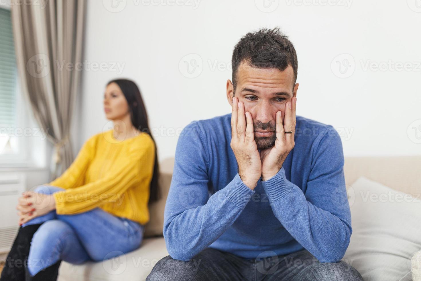 un jeune homme assis sur un canapé se dispute avec sa petite amie qui a la tête détournée. couple assis sur le canapé ne parlant pas après une bagarre à la maison dans le salon photo