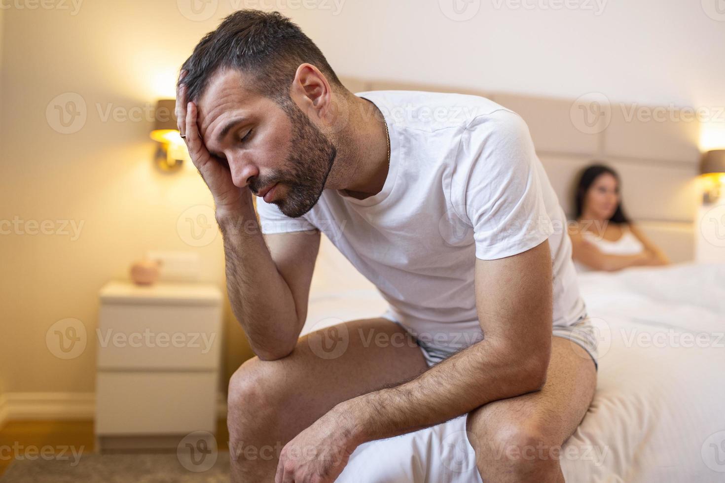 jeune couple en crise relationnelle, homme et femme bouleversés assis séparés sur le lit, espace vide entre eux photo