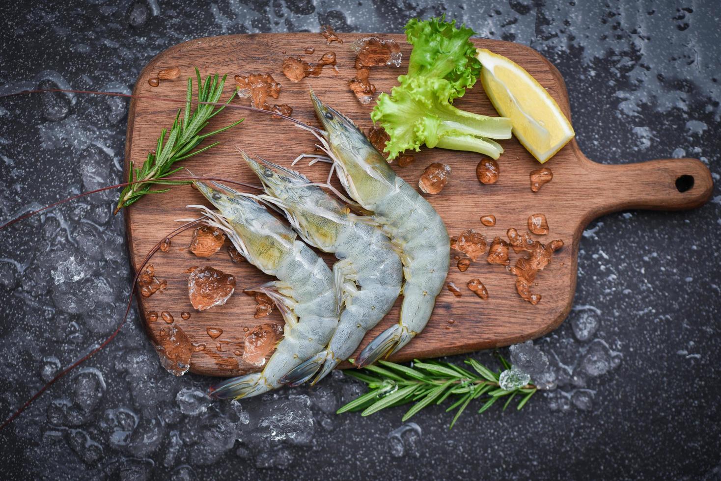 crevettes fraîches sur une planche à découper en bois avec des ingrédients de romarin herbes et épices pour la cuisson des fruits de mer crevettes crues crevettes sur glace congelées au restaurant de fruits de mer photo