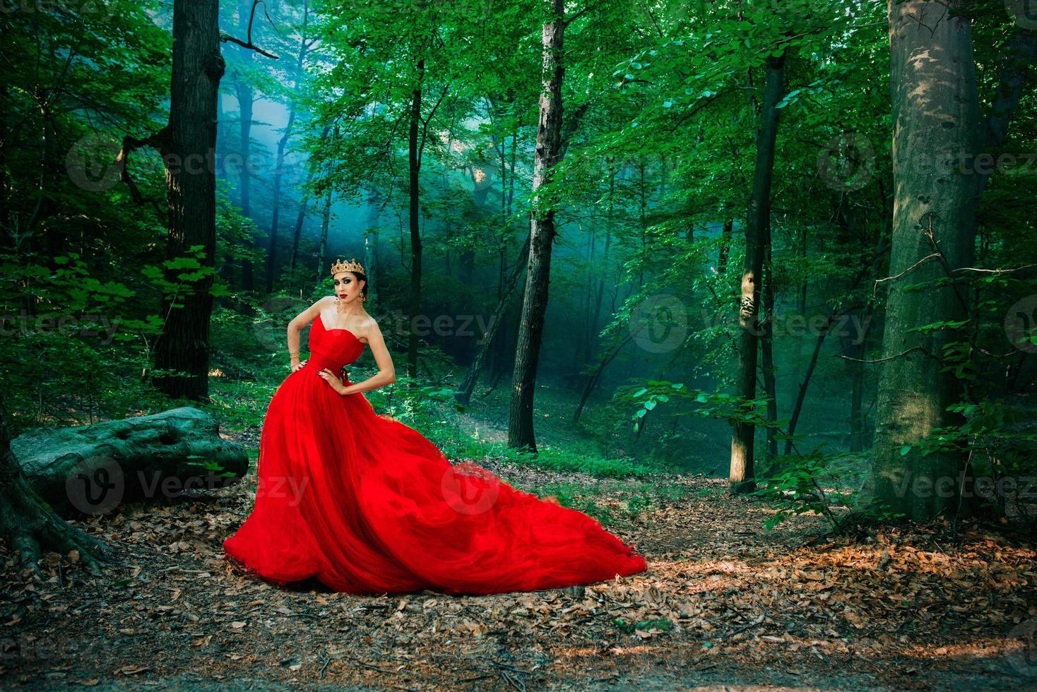 élégante femme élégante dans une longue robe rouge et une couronne royale dans la forêt brumeuse photo