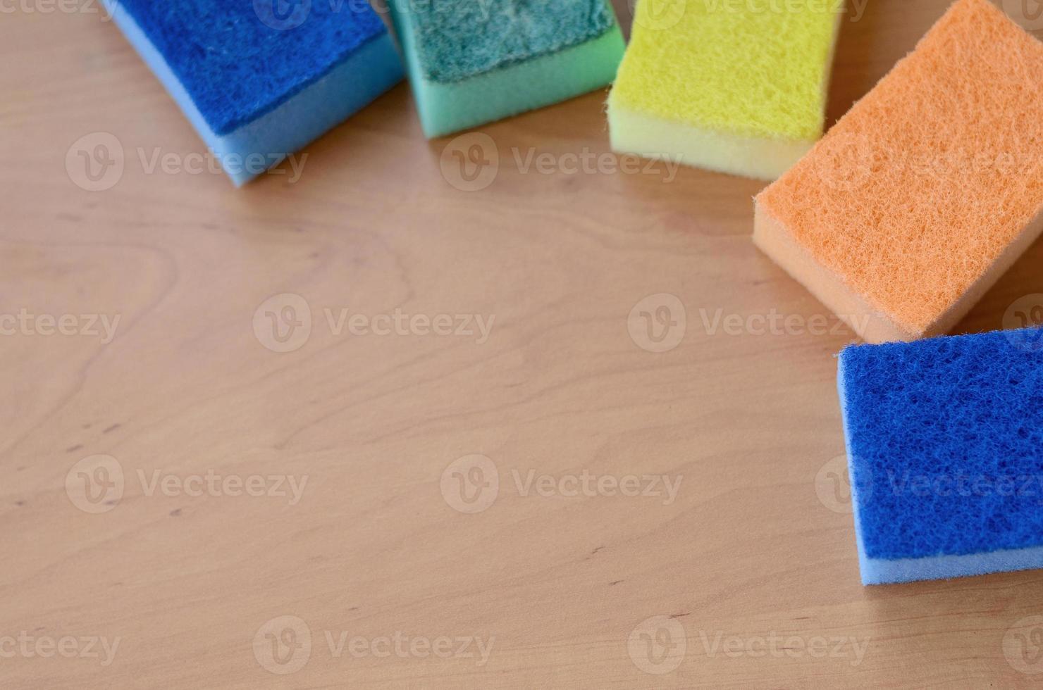 quelques éponges de cuisine reposent sur un comptoir de cuisine en bois. des objets colorés pour laver la vaisselle et nettoyer dans la maison sont prêts à l'emploi photo