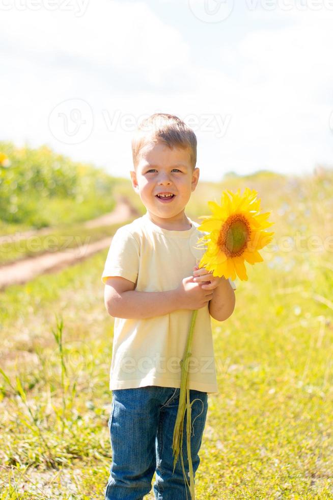 petit garçon mignon dans un champ de tournesols dans un t-shirt jaune se dresse et sourit. photo