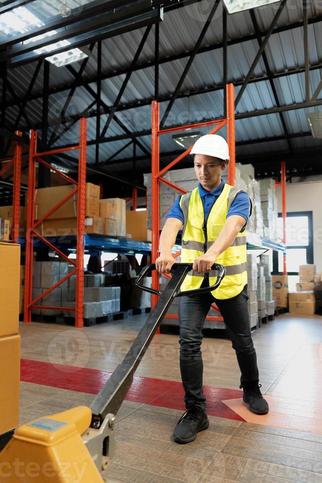 portrait, travailleur d'entrepôt masculin asiatique du millénaire fatigué tirant un transpalette, souffrant de maux de dos, travaillant dans un entrepôt. photo