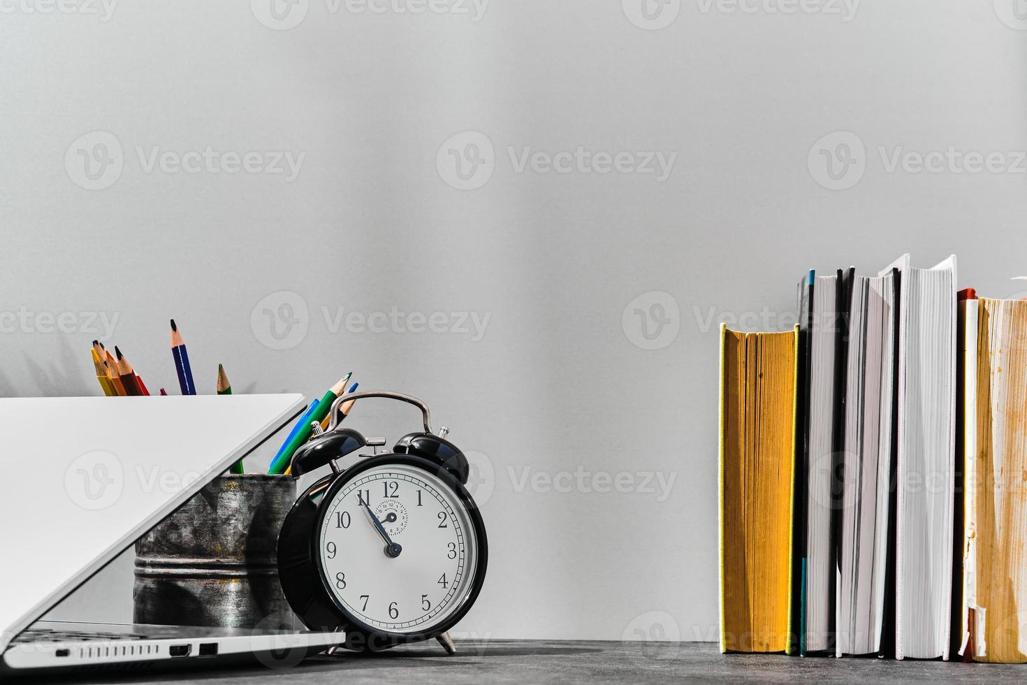 concept retour à l'école ou idée de la journée des enseignants. stylos, crayons, livres, réveil et ordinateur portable sur la table, sur fond de tableau gris. retour à l'école, avec espace de copie. photo