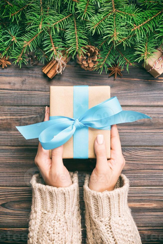 mains féminines tenant une boîte cadeau faite à la main en papier recyclé sur fond vintage de table en bois foncé. concept de préparation de noël, fond d'emballage cadeau photo