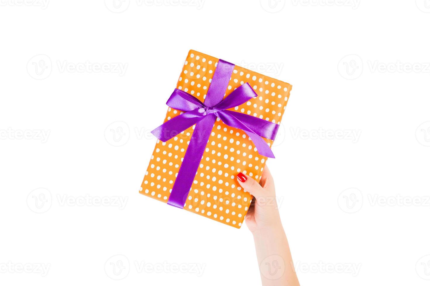les mains de la femme donnent un cadeau de noël enveloppé ou d'autres vacances faites à la main dans du papier orange avec un ruban violet. isolé sur fond blanc, vue de dessus. concept de boîte-cadeau d'action de grâces photo