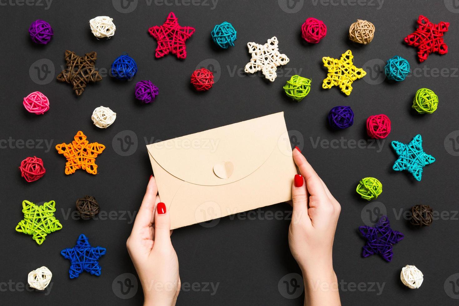 vue de dessus d'une femme tenant une enveloppe sur fond noir faite de décorations de vacances. notion de temps de noël photo