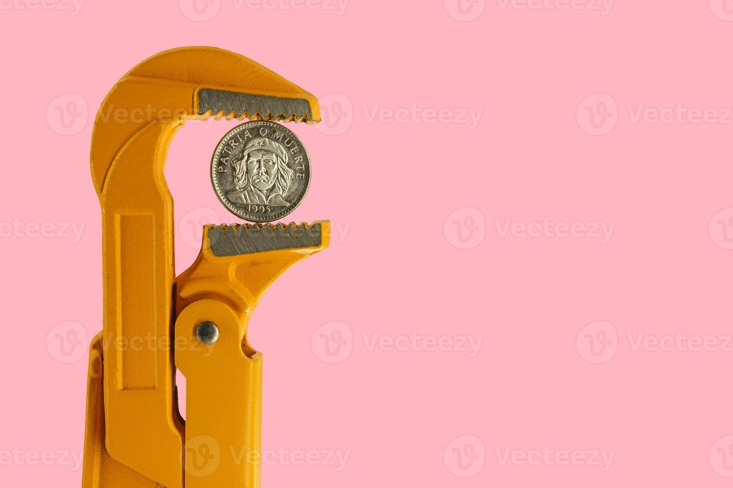 Pièce de trois pesos cubains tenue dans une clé de plombier orange sur fond rose photo