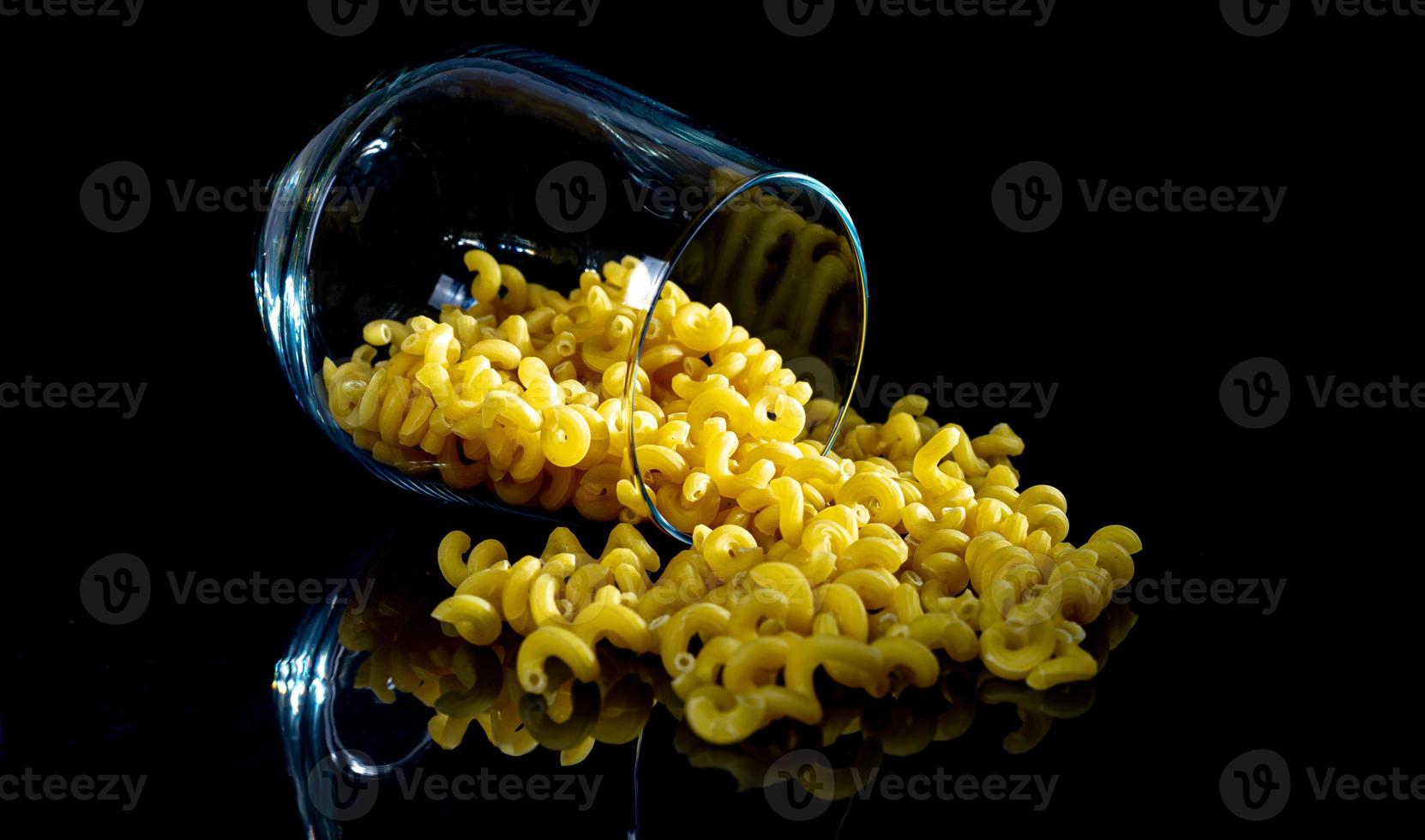 pâtes crues dans un bocal en verre, verre à vin. en seau. pâtes crues sur fond noir. vue de face pâtes crues, tombées de la main, place pour le texte, longues pailles de spaghetti jaunes, photo