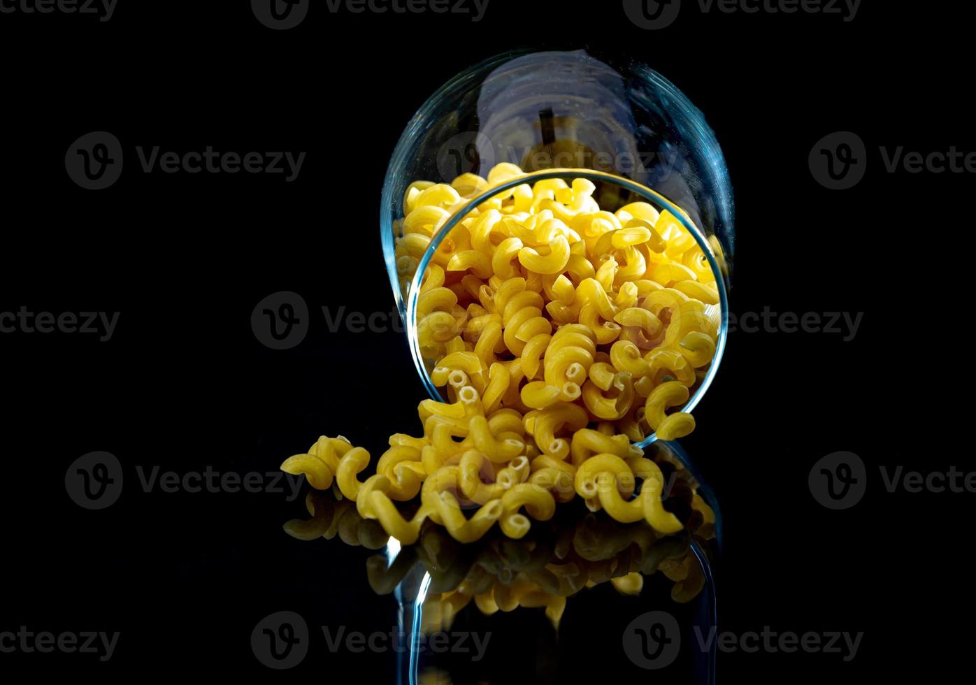 pâtes crues dans un bocal en verre, verre à vin. en seau. pâtes crues sur fond noir. vue de face pâtes crues, tombées de la main, place pour le texte, longues pailles de spaghetti jaunes, photo