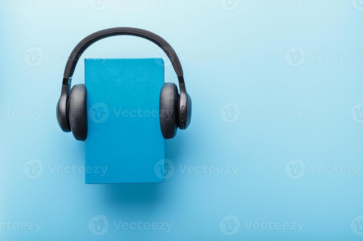 les écouteurs sont portés sur un livre dans une couverture rigide bleue sur fond bleu, vue de dessus. photo