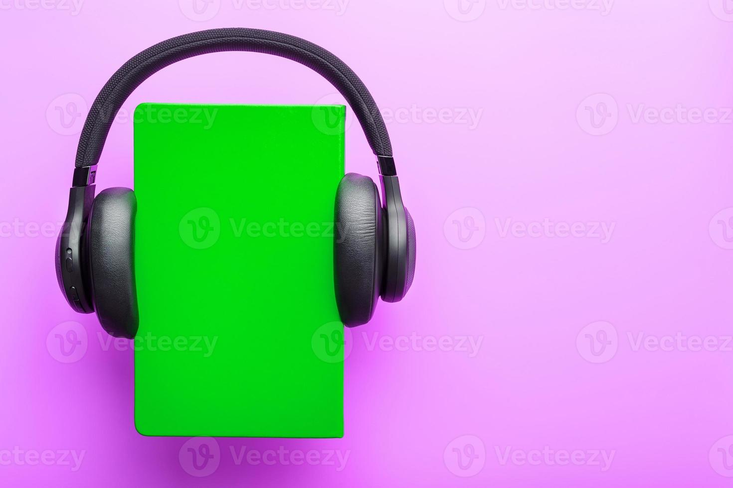 les écouteurs sont portés sur un livre dans une couverture rigide verte sur fond lilas, vue de dessus. photo