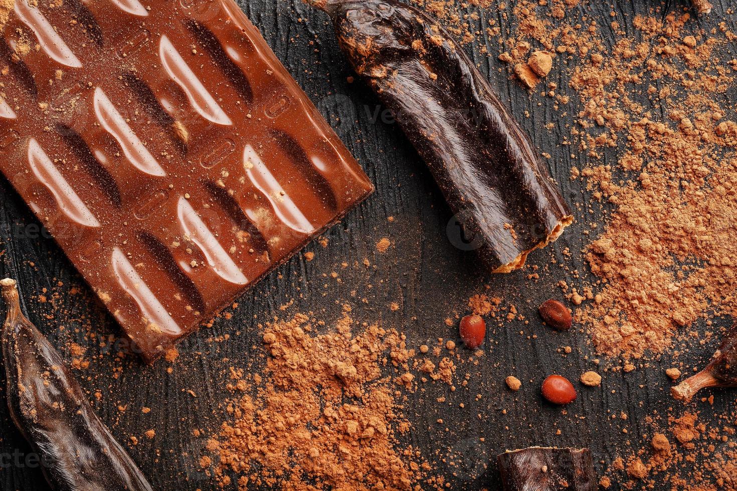 les gousses de la barre de chocolat caroube sur fond noir. bonbons, chocolat et confiserie à base de caroube. photo