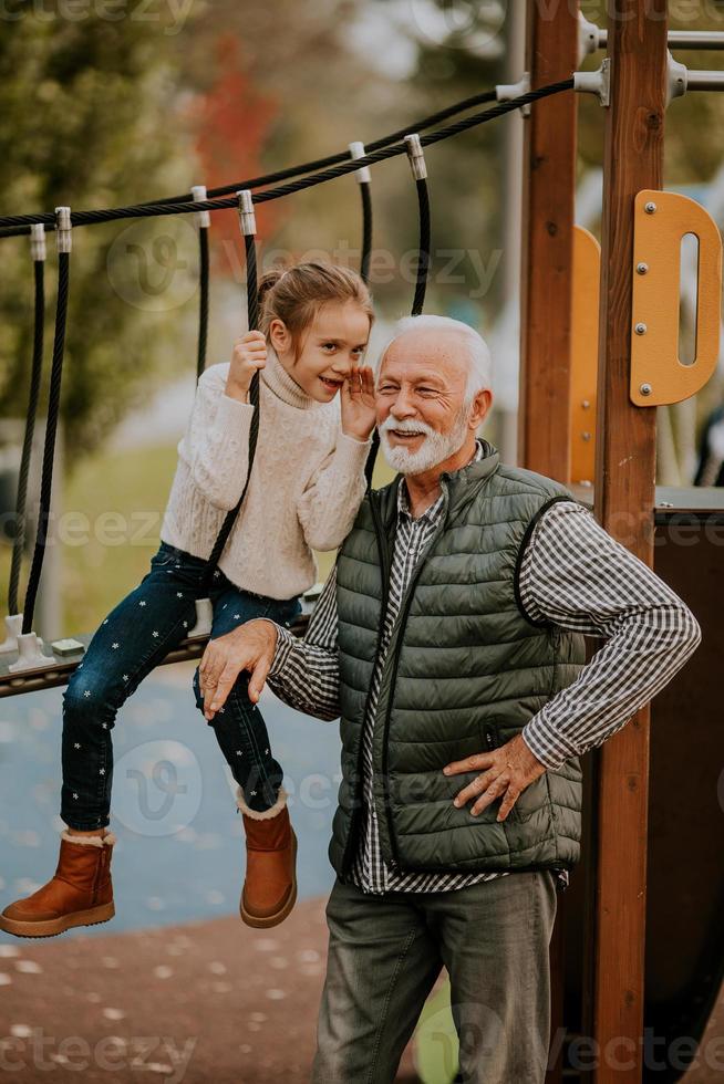 grand-père passe du temps avec sa petite-fille dans l'aire de jeux du parc le jour de l'automne photo