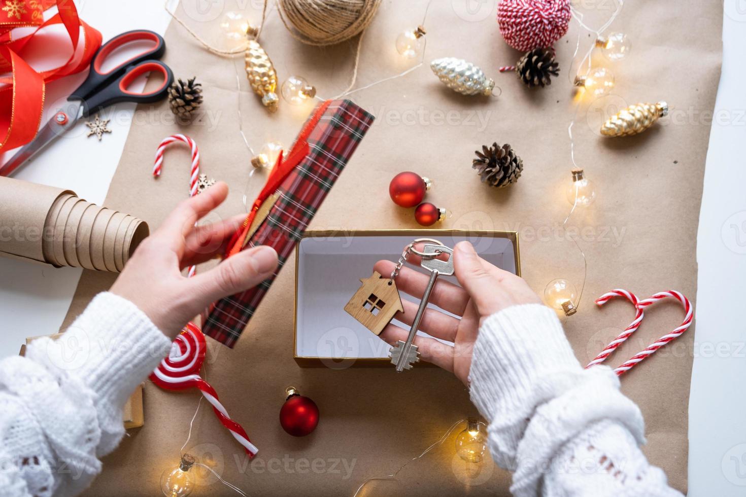 clé de la maison avec porte-clés sur une maison confortable dans une boîte cadeau avec emballage de décoration de noël. pack cadeau pour le nouvel an, noël. construction, projet, emménagement dans une nouvelle maison, hypothèque, location, achat immobilier photo