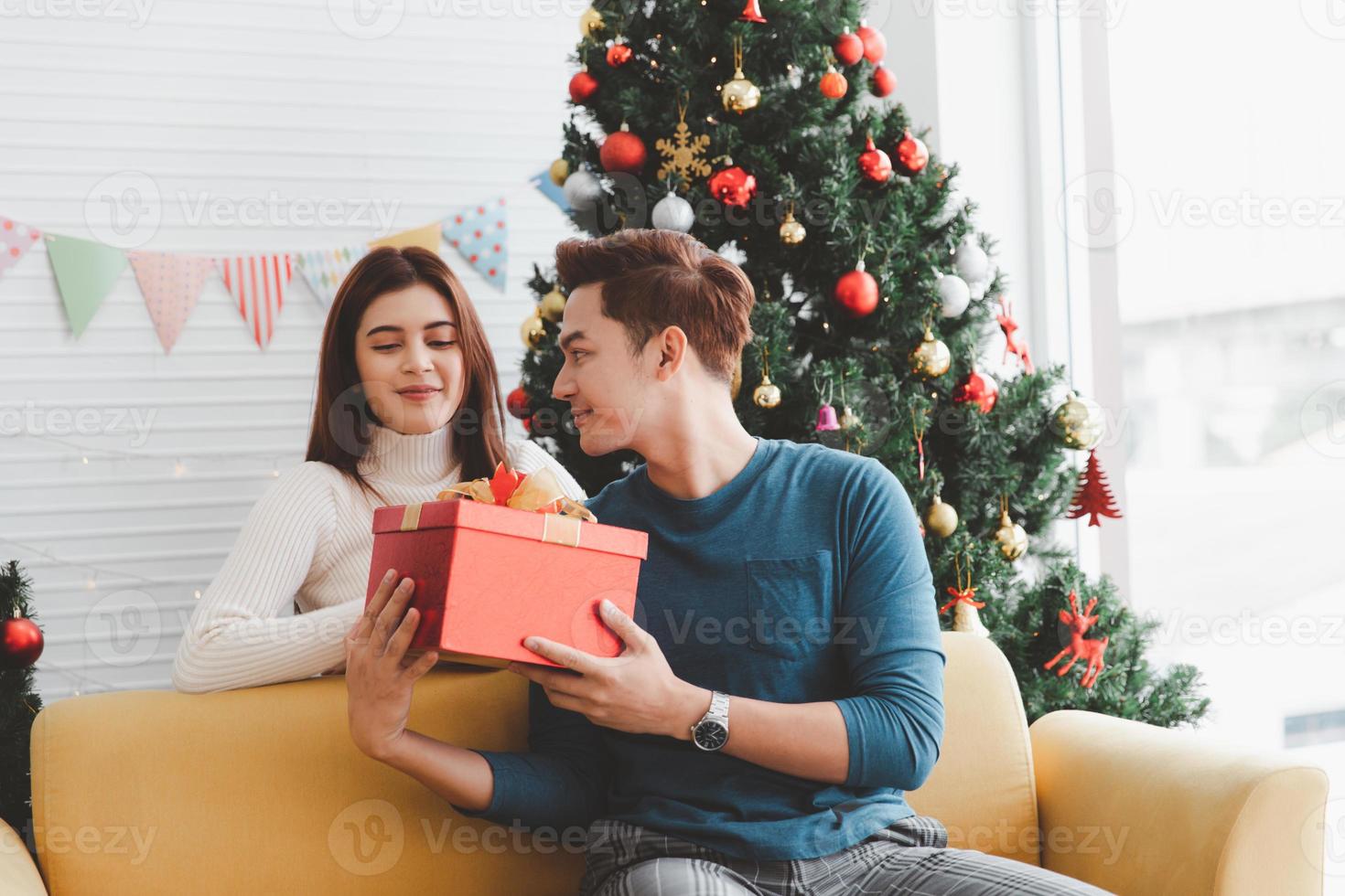 un homme donne des cadeaux à une femme dans un salon décoré d'un sapin de noël pendant le nouvel an et noël photo