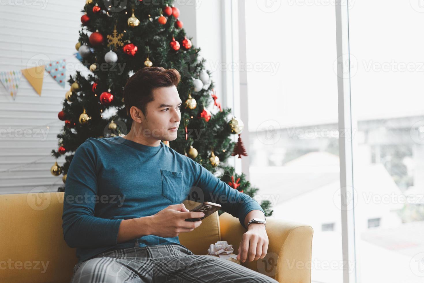 un homme seul semble seul utilisant son téléphone dans son salon décoré d'arbres de noël photo