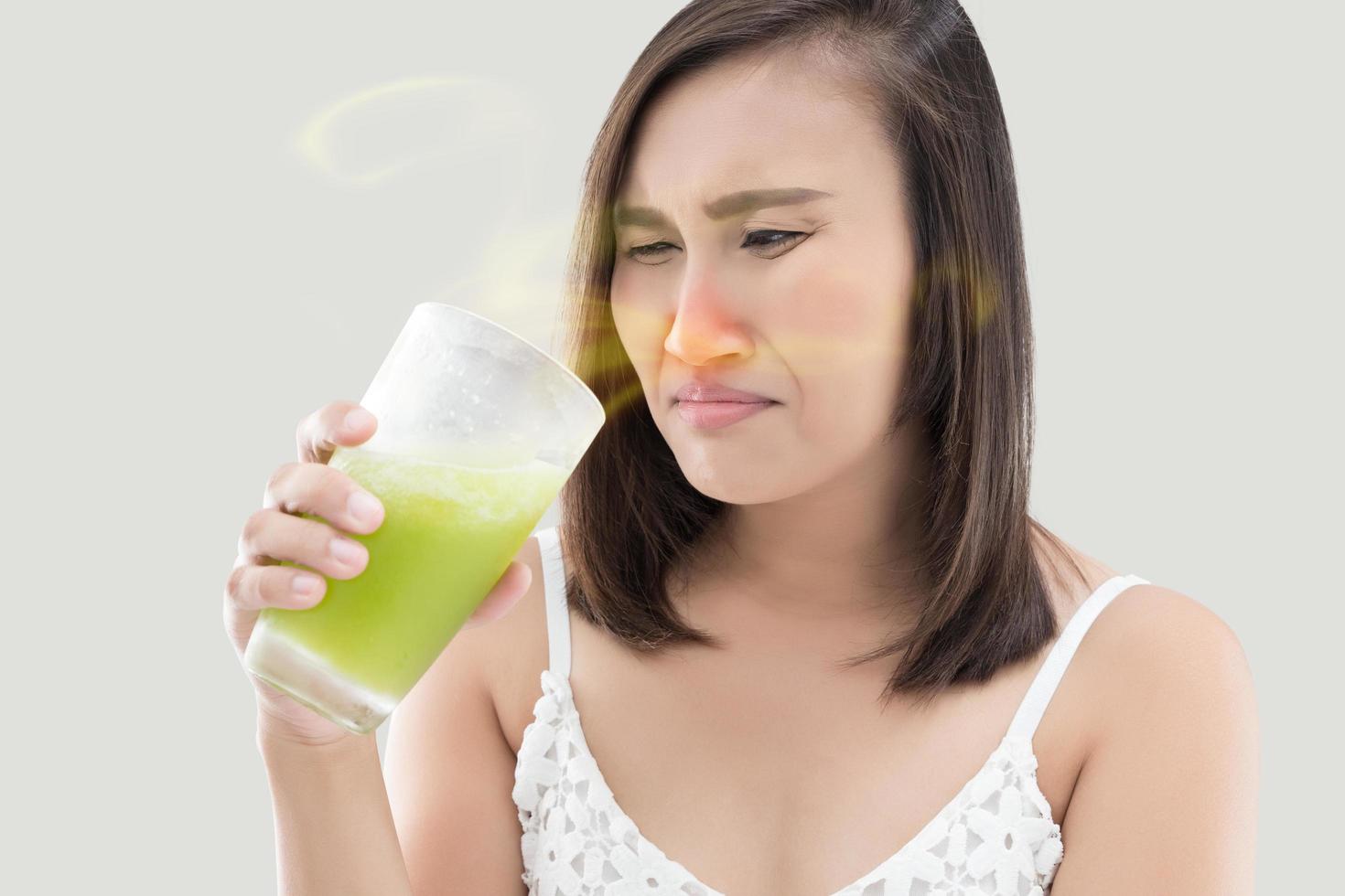 la femme asiatique est dégoûtée du jus sur fond gris. pas délicieux, congestion nasale. photo