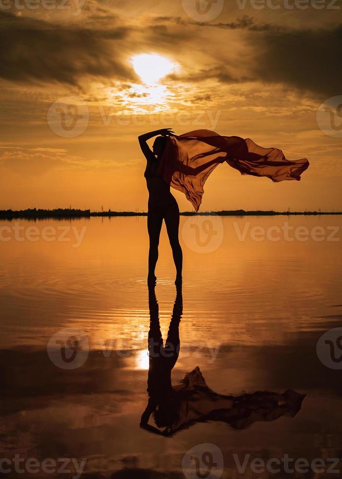 silhouette d'une jeune fille en maillot de bain rouge sur la plage. un tissu rouge se développe dans ses mains. photo