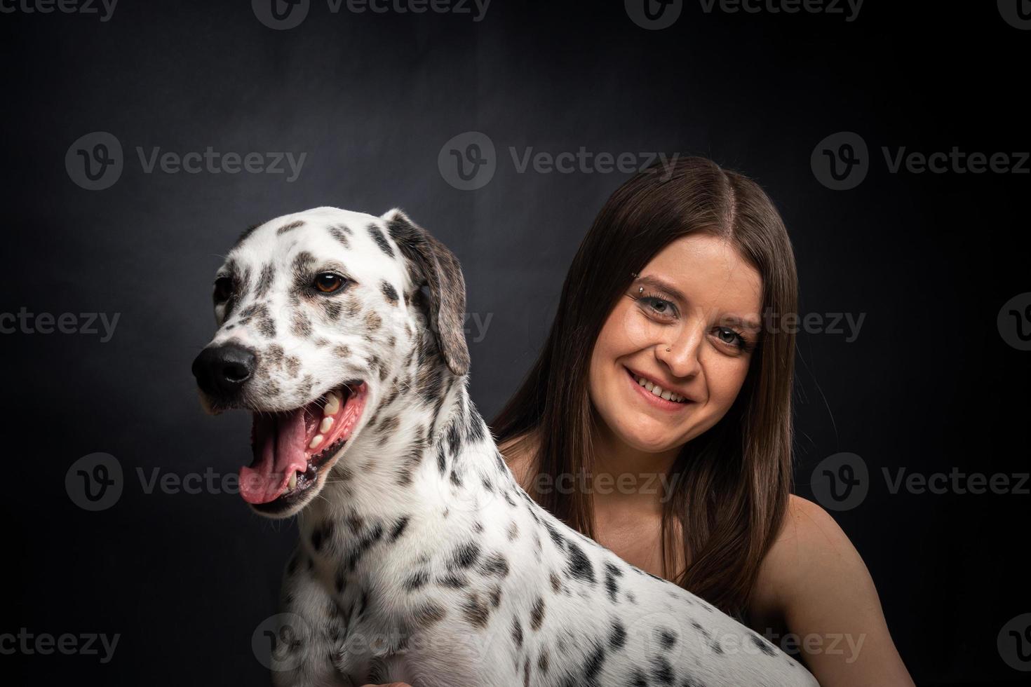 une jeune jolie femme joue avec son animal de compagnie dalmatien, isolé sur fond noir. photo