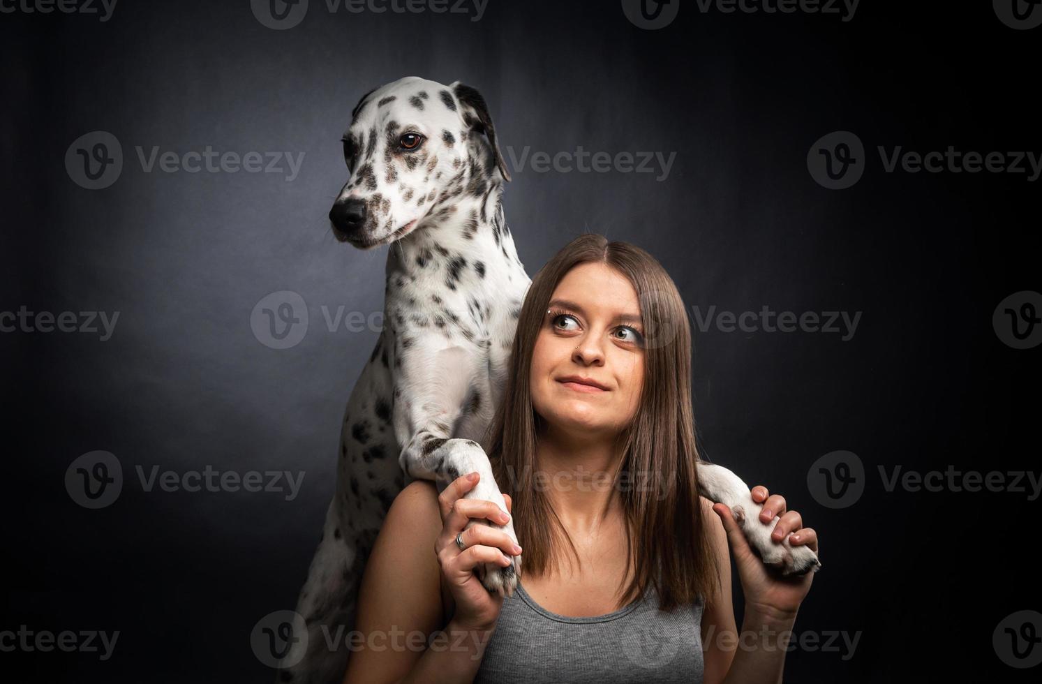 une jeune jolie femme joue avec son animal de compagnie dalmatien, isolé sur fond noir. photo