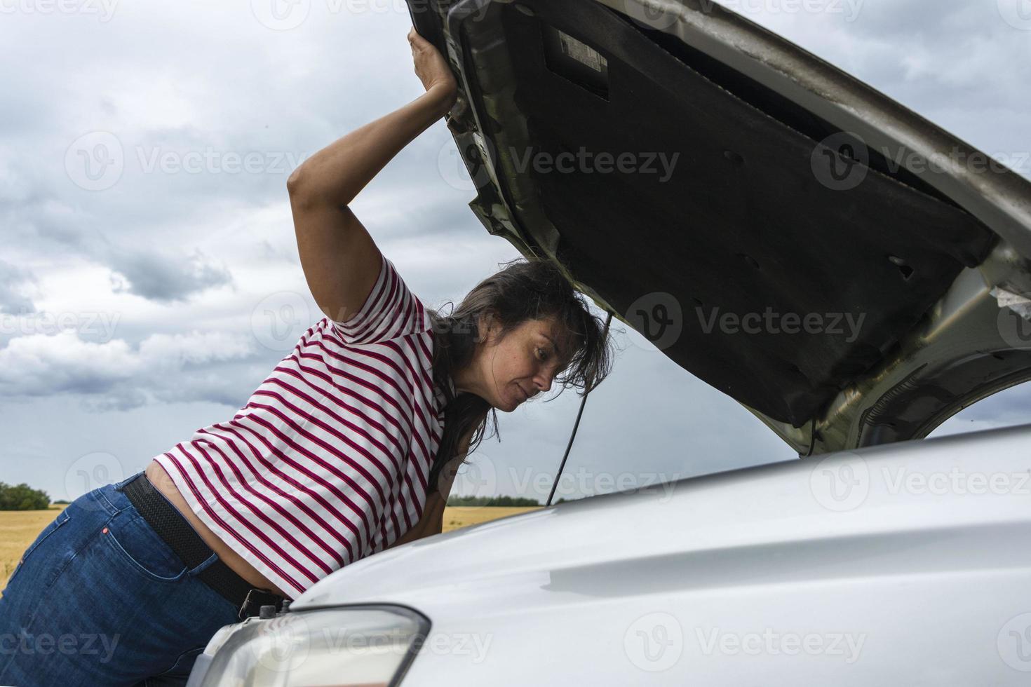 une voiture cassée. une jeune femme se tient sur la route près d'une voiture cassée au milieu de nulle part. j'ai besoin d'aide. photo