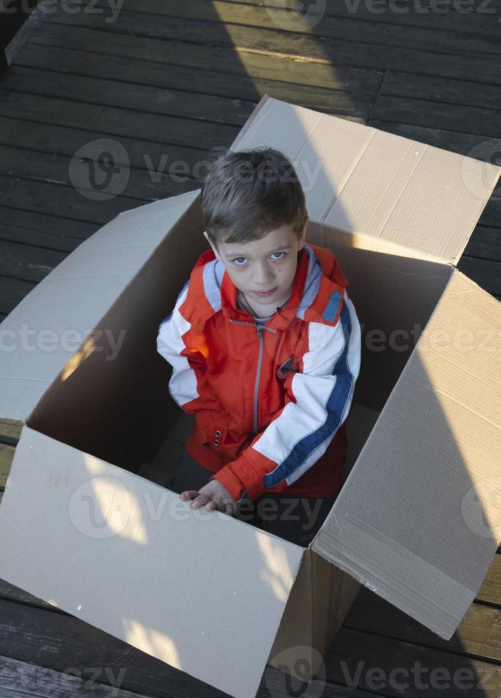 mignon garçon européen jetant un coup d'œil hors d'une boîte en carton, cadeau, surprise, vie sans-abri, emballage, jeu de cache-cache photo