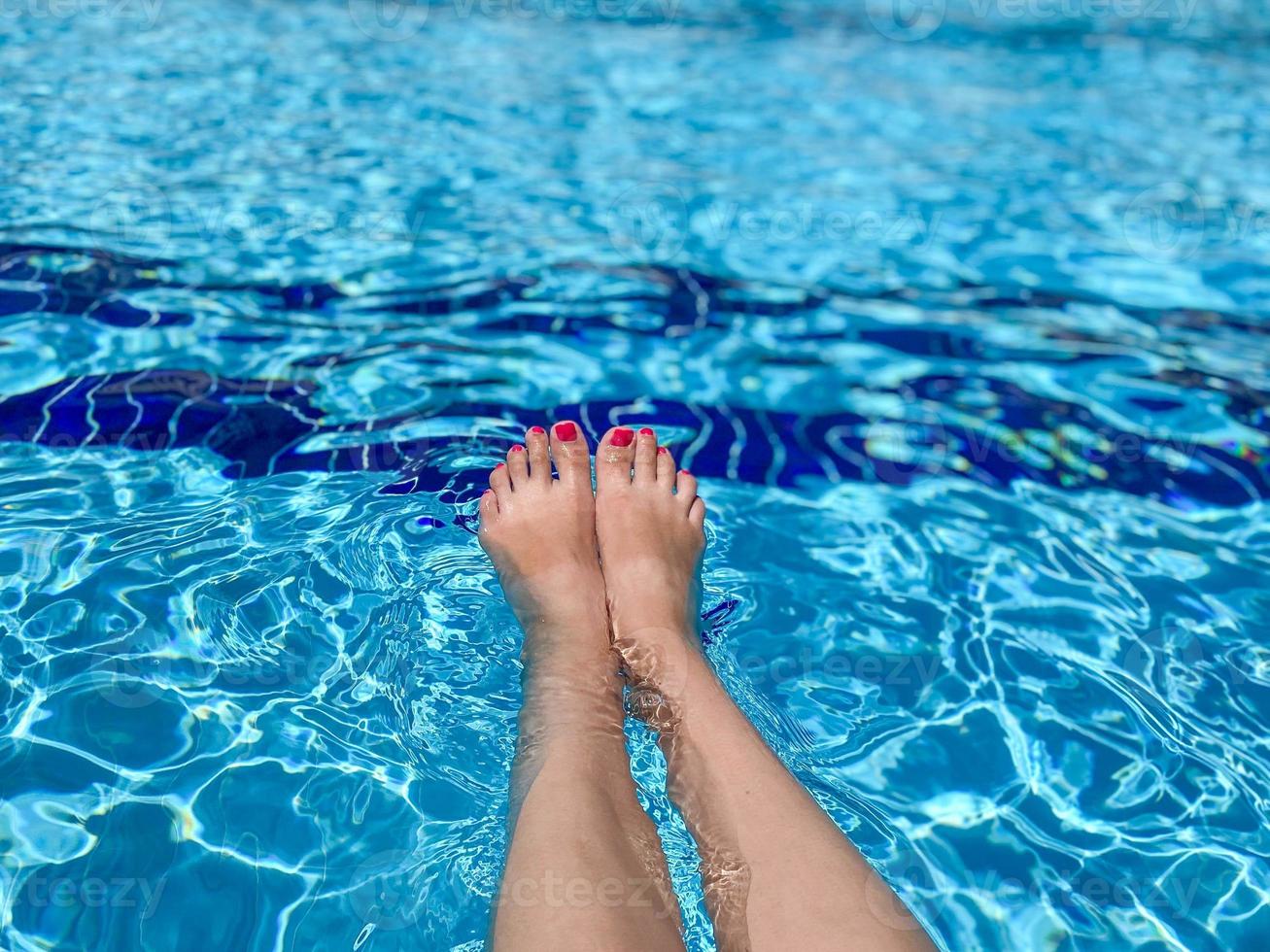 les pieds dans l'eau de la piscine. selfie des jambes et des pieds nus avec des ongles de pédicure et de manucure rouges sur fond de mer bleue. vacances aux vacances d'été photo