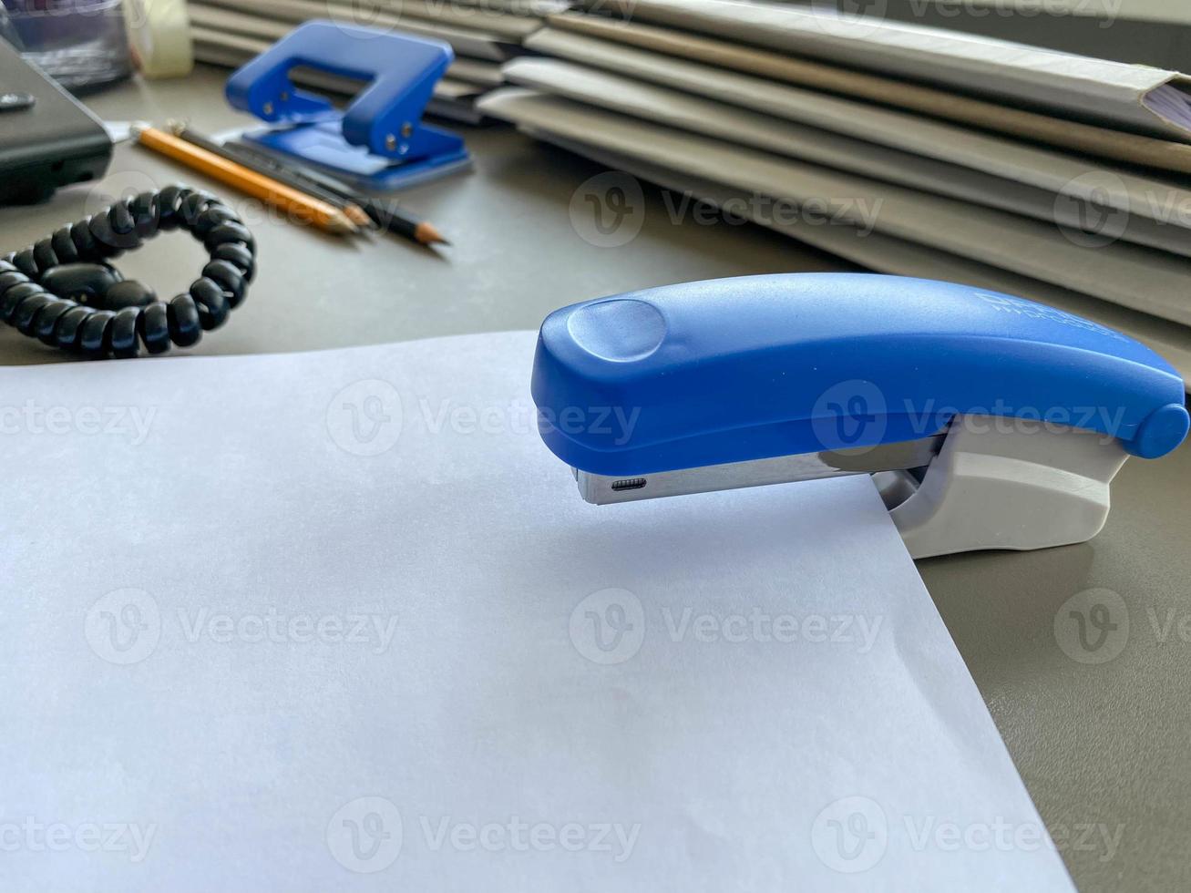 une grande agrafeuse bleue pour agrafer le papier se trouve à côté des dossiers de documents sur le bureau de travail du bureau. papeterie photo