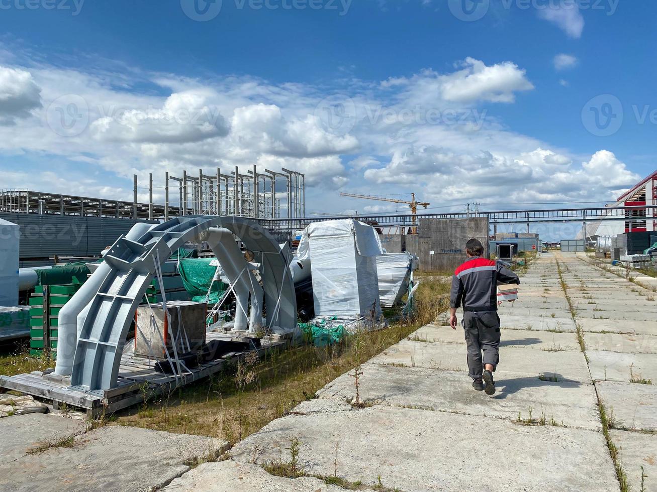 un ingénieur de travail masculin traverse un entrepôt d'équipements et de matériaux industriels dans des boîtes dans une zone de stockage en plein air. vue de dos photo