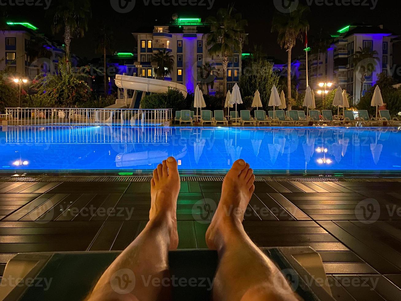 Les pieds des hommes sur une chaise longue au bord de la piscine la nuit dans un hôtel dans un pays tropical chaud de l'Est Southern Paradise Resort photo