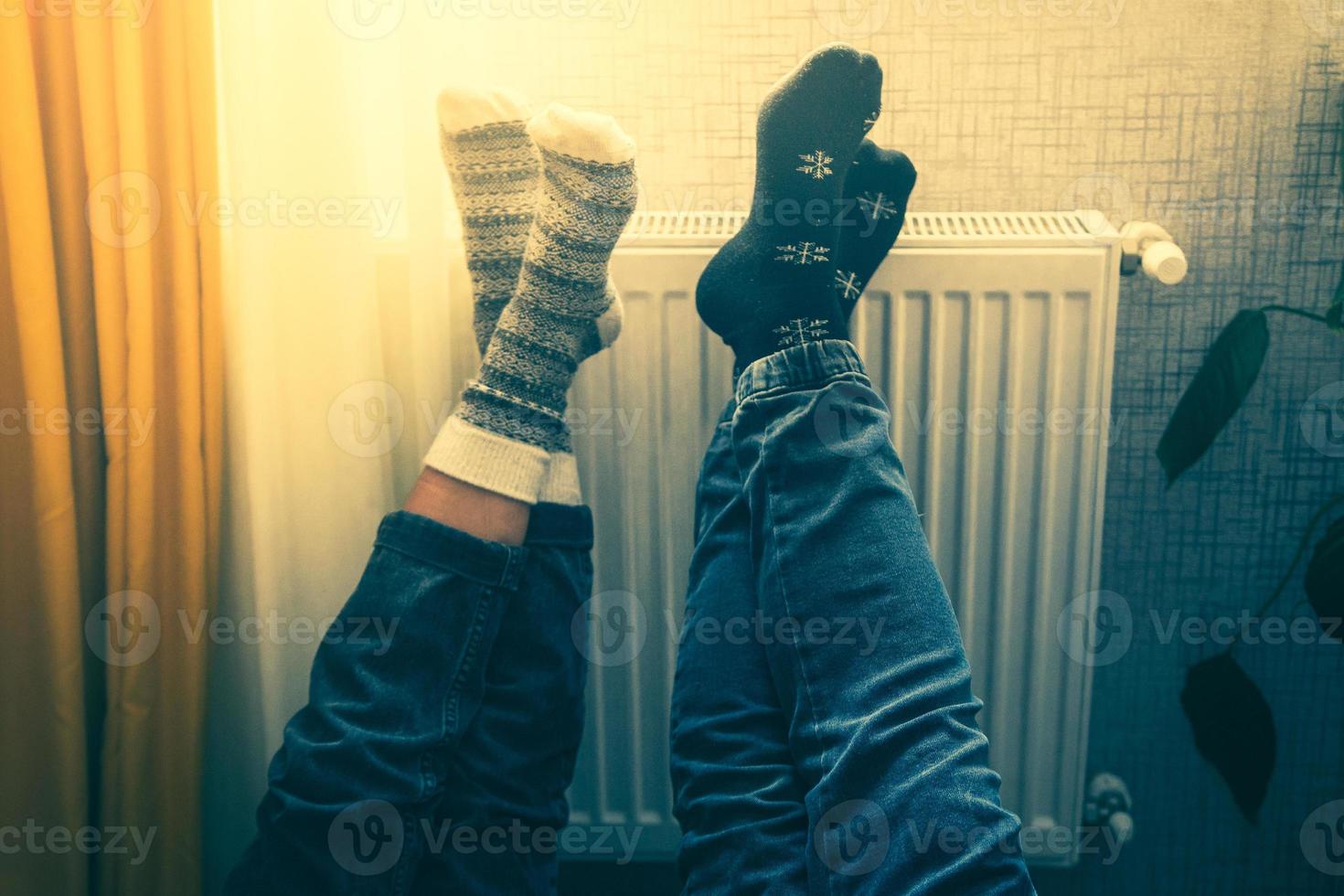 un couple tient les jambes en l'air chauffant les pieds dans une maison froide à l'intérieur sur un radiateur en hiver avec des chaussettes en laine élégantes pour l'hiver. valentines drôle ensemble pieds chauds par radiateur par fenêtre photo