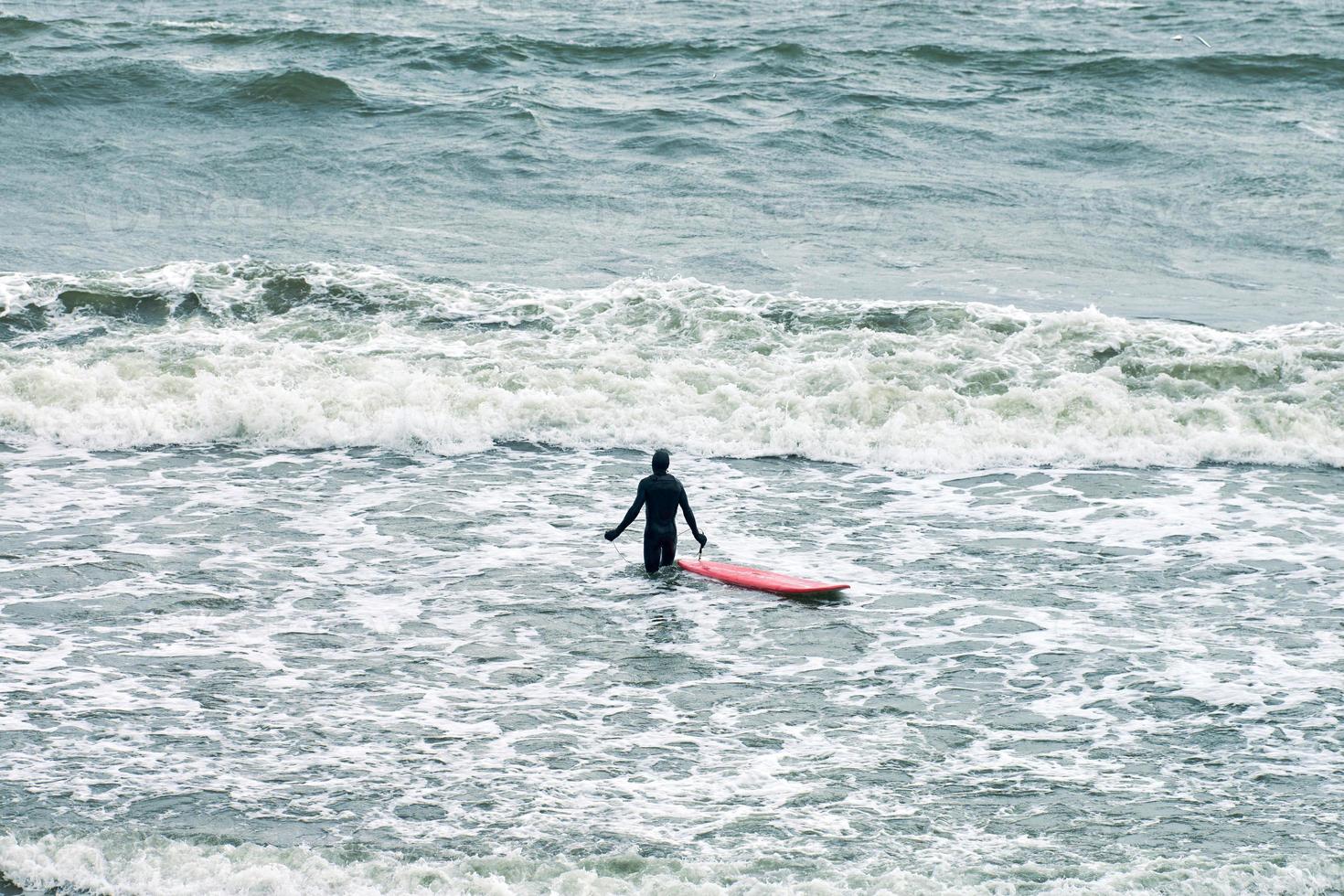 surfeur masculin en maillot de bain en mer avec planche de surf rouge photo