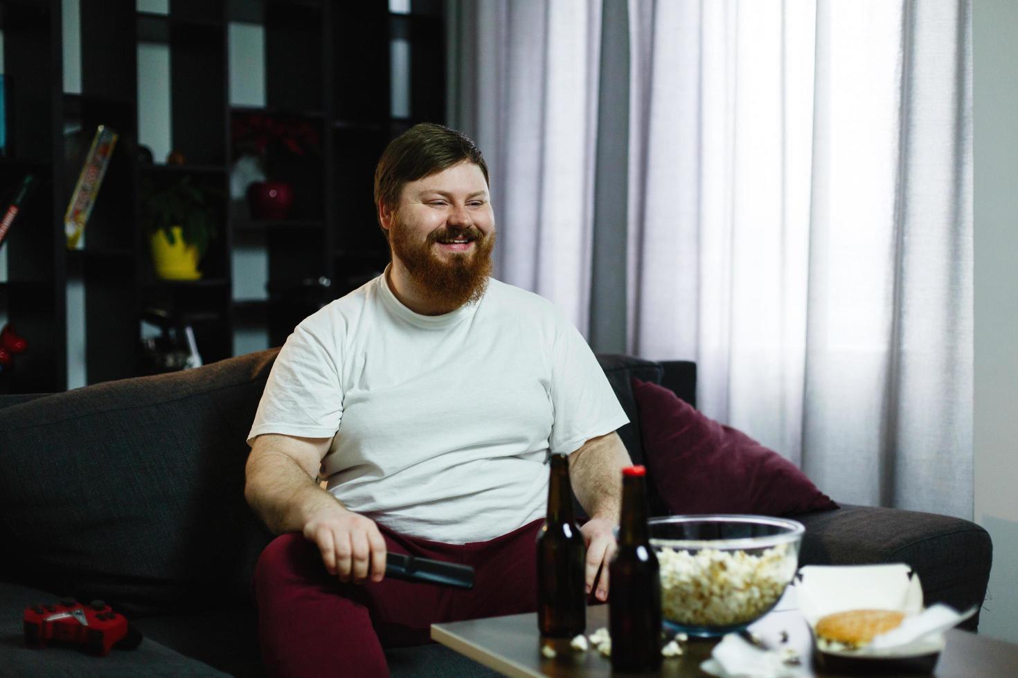 L'homme sourit assis sur le canapé avec des collations photo