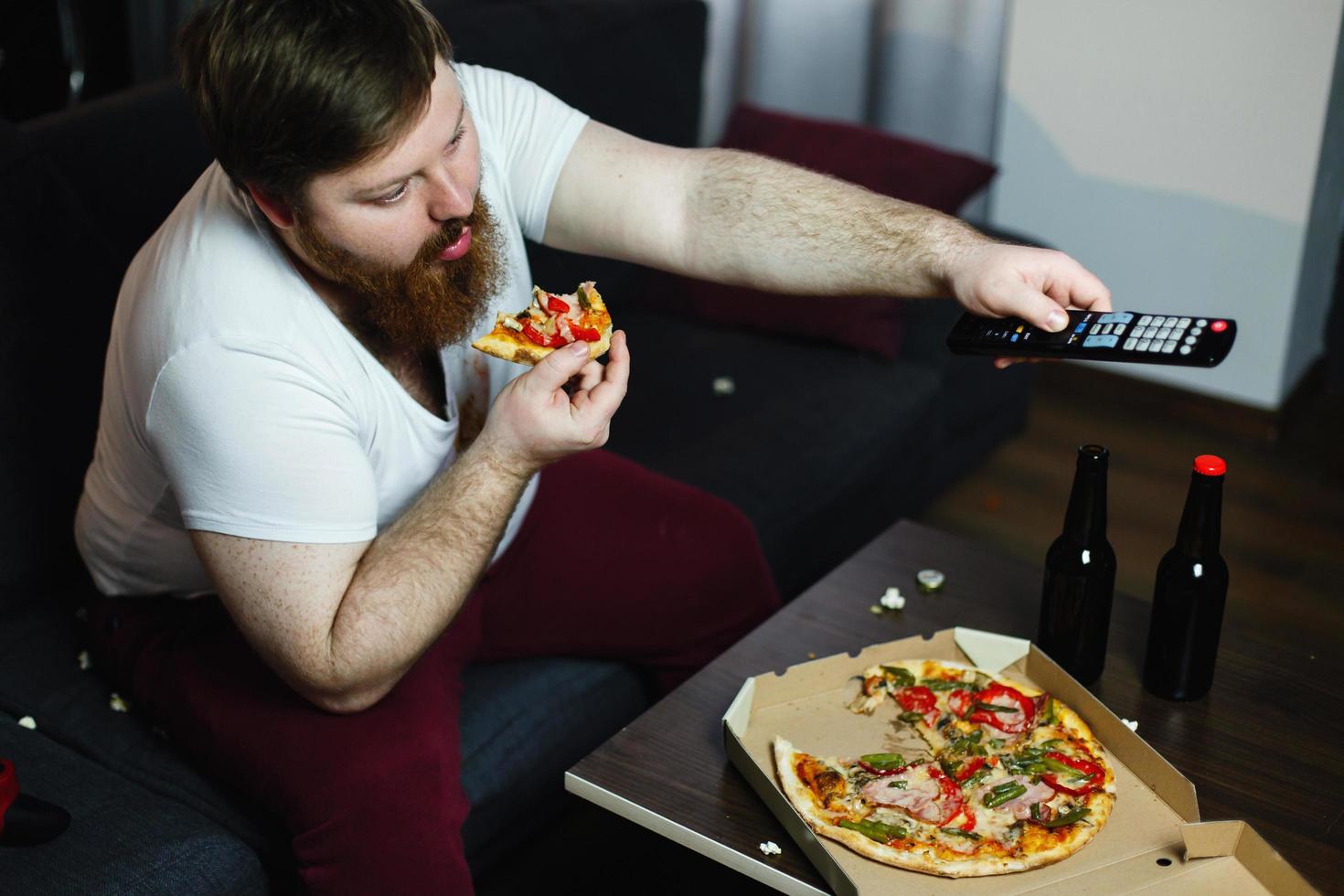 gros homme mange de la pizza assis sur le canapé photo