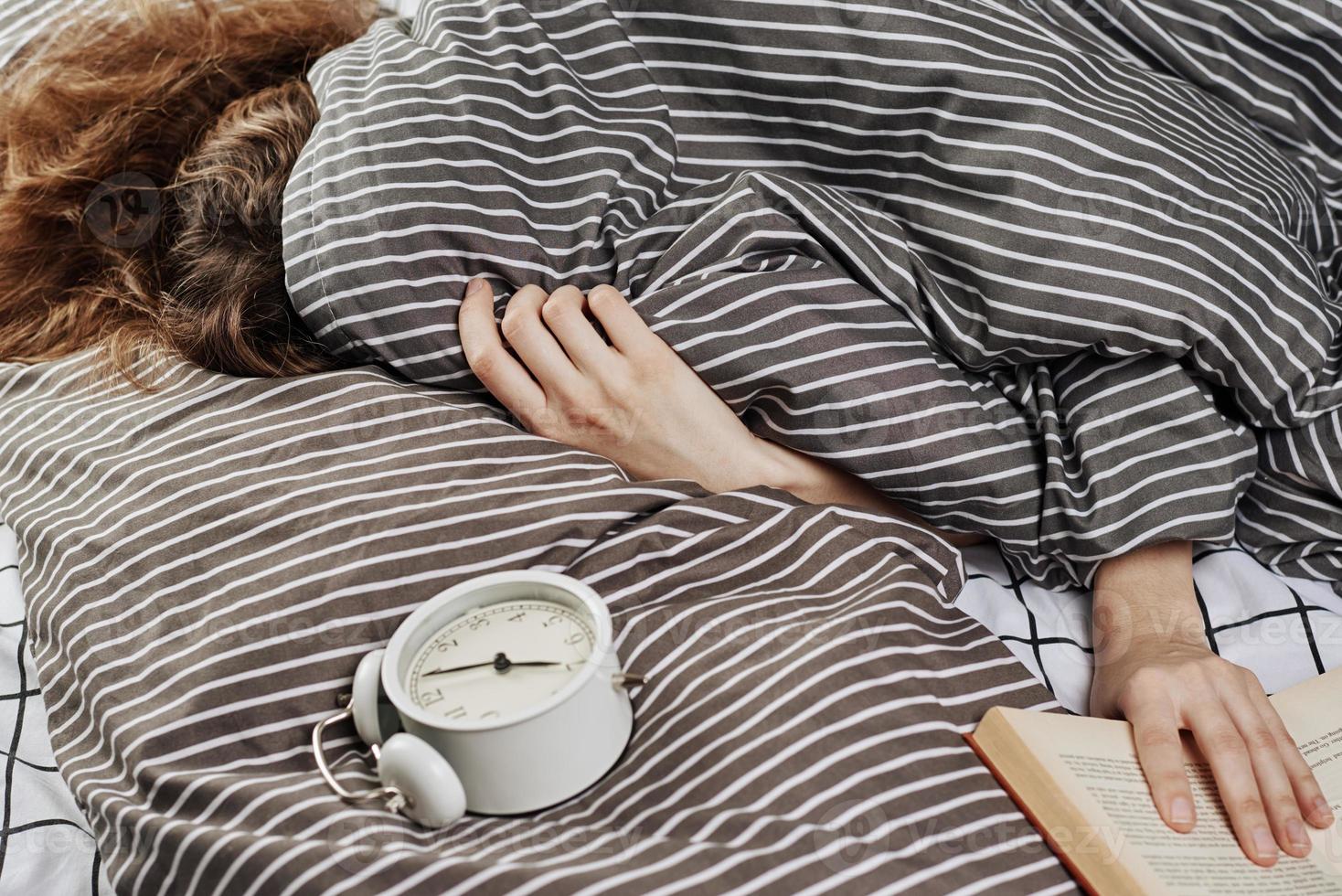 femme endormie couverte sous couverture dans son lit et réveil vintage sur oreiller. photo