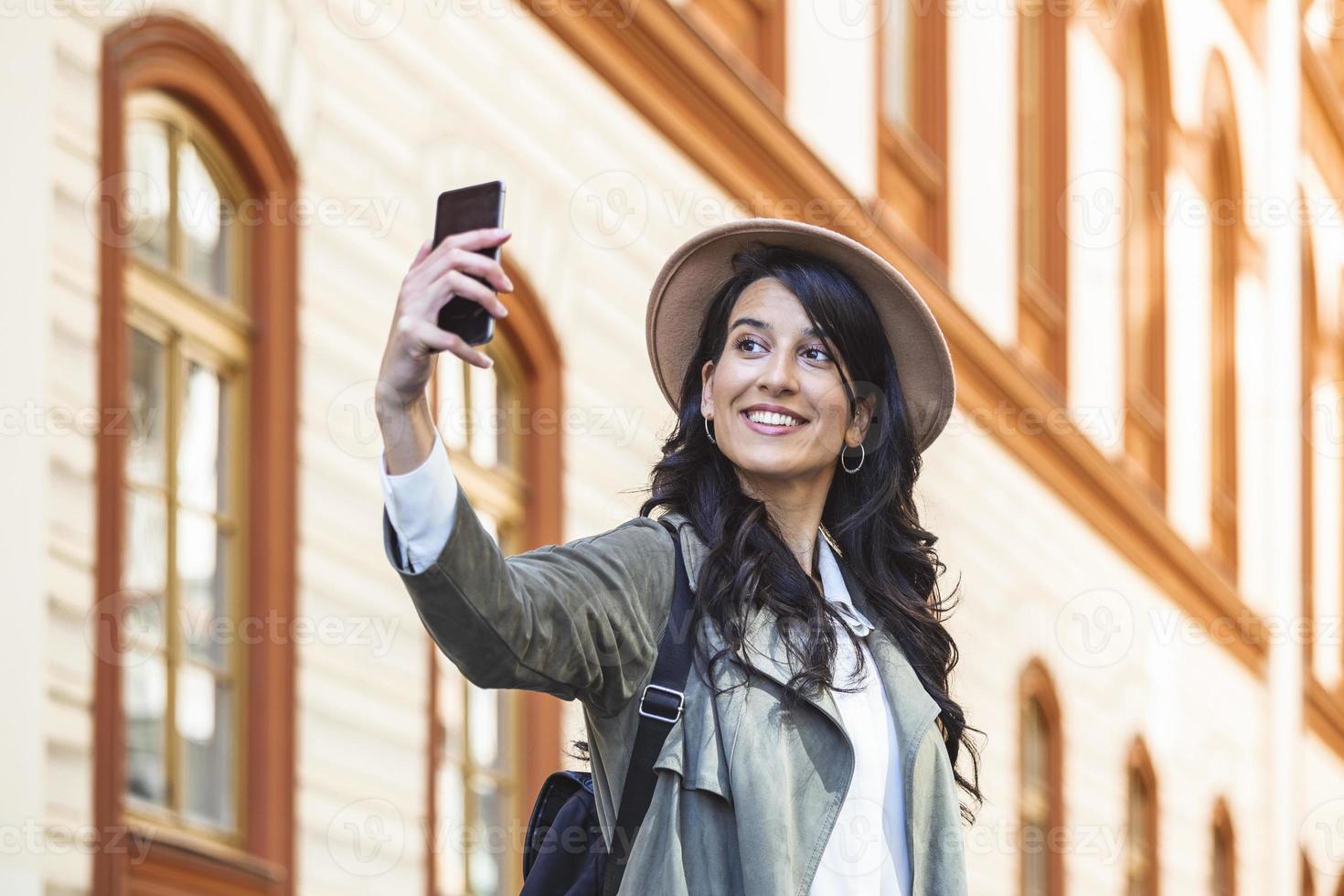 touriste posant pour un selfie dans une rue. vlogger enregistrant du contenu pour son vlog de voyage. jolie jeune fille souriante fait selfie sur un appareil photo tout en marchant à l'extérieur.