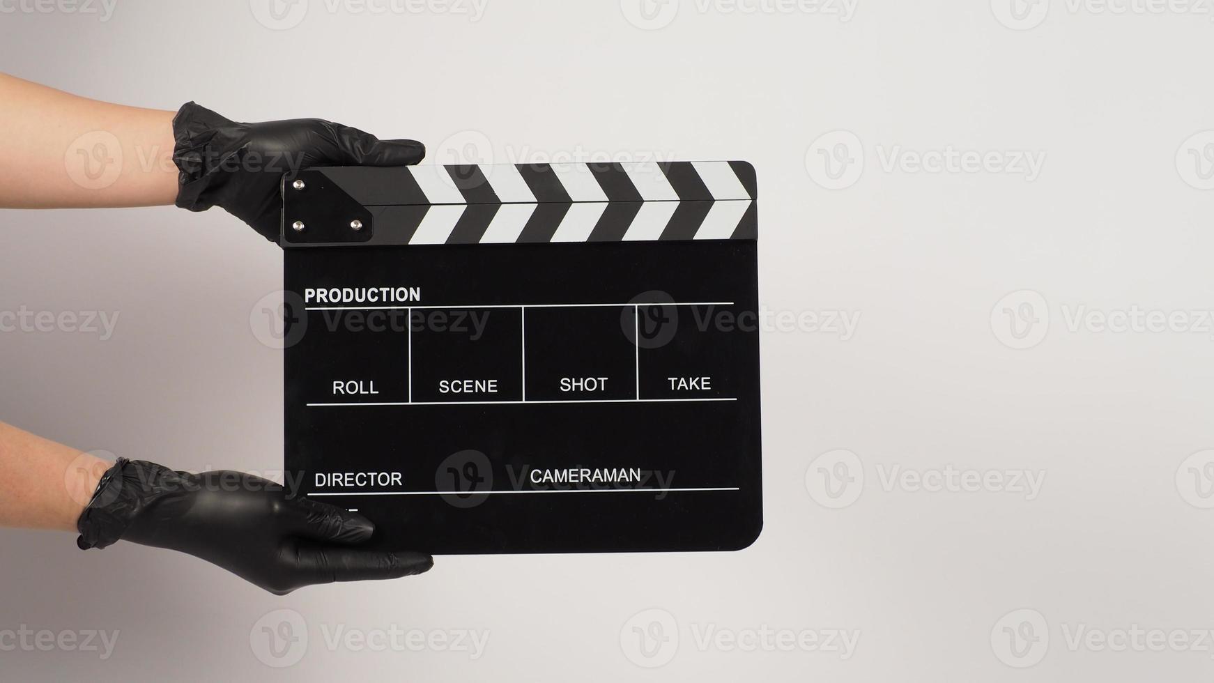 tenir à la main un panneau de clapet noir ou une ardoise de film et porter un gant en latex noir sur fond blanc. photo