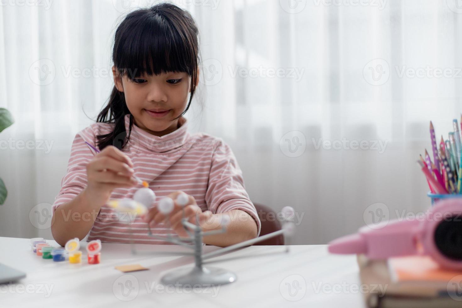 une petite fille asiatique étudie le système solaire en cours de géographie. en regardant le modèle à l'échelle des planètes photo