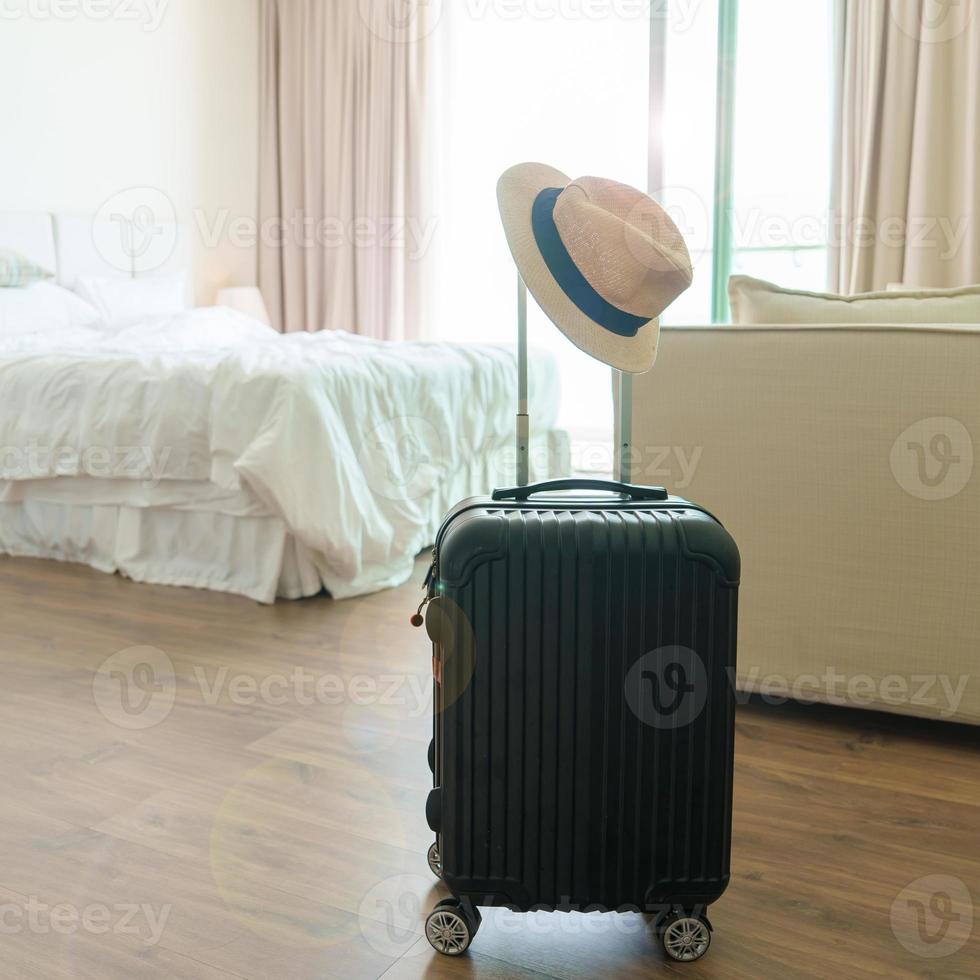 bagage noir avec chapeau dans une chambre d'hôtel moderne après l'ouverture de la porte. bagages pour le temps de voyager, service, voyage, voyage, vacances d'été et concepts de vacances photo