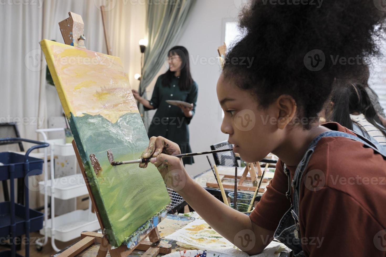 une fille afro-américaine se concentre sur la peinture acrylique sur toile avec un groupe d'étudiants en classe d'art, l'apprentissage créatif avec des talents et des compétences dans l'enseignement en studio à l'école primaire. photo