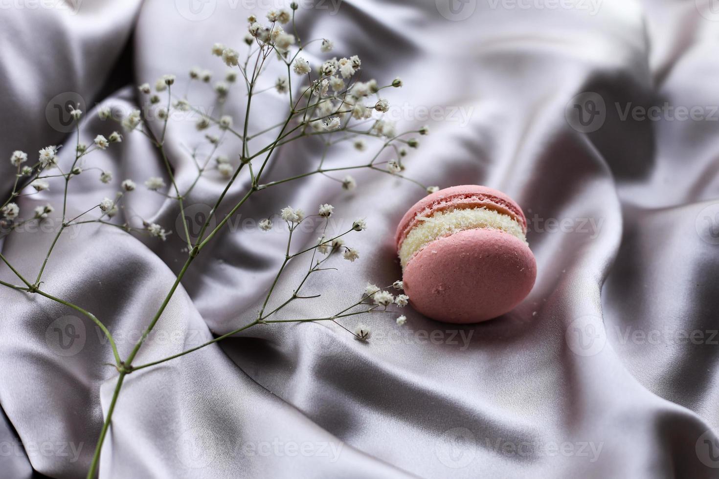macarons français roses ou biscuits macarons et fleurs blanches sur fond de tissu. arômes naturels de fruits et de baies, farce crémeuse pour la saint-valentin fête des mères pâques avec de la nourriture d'amour. photo