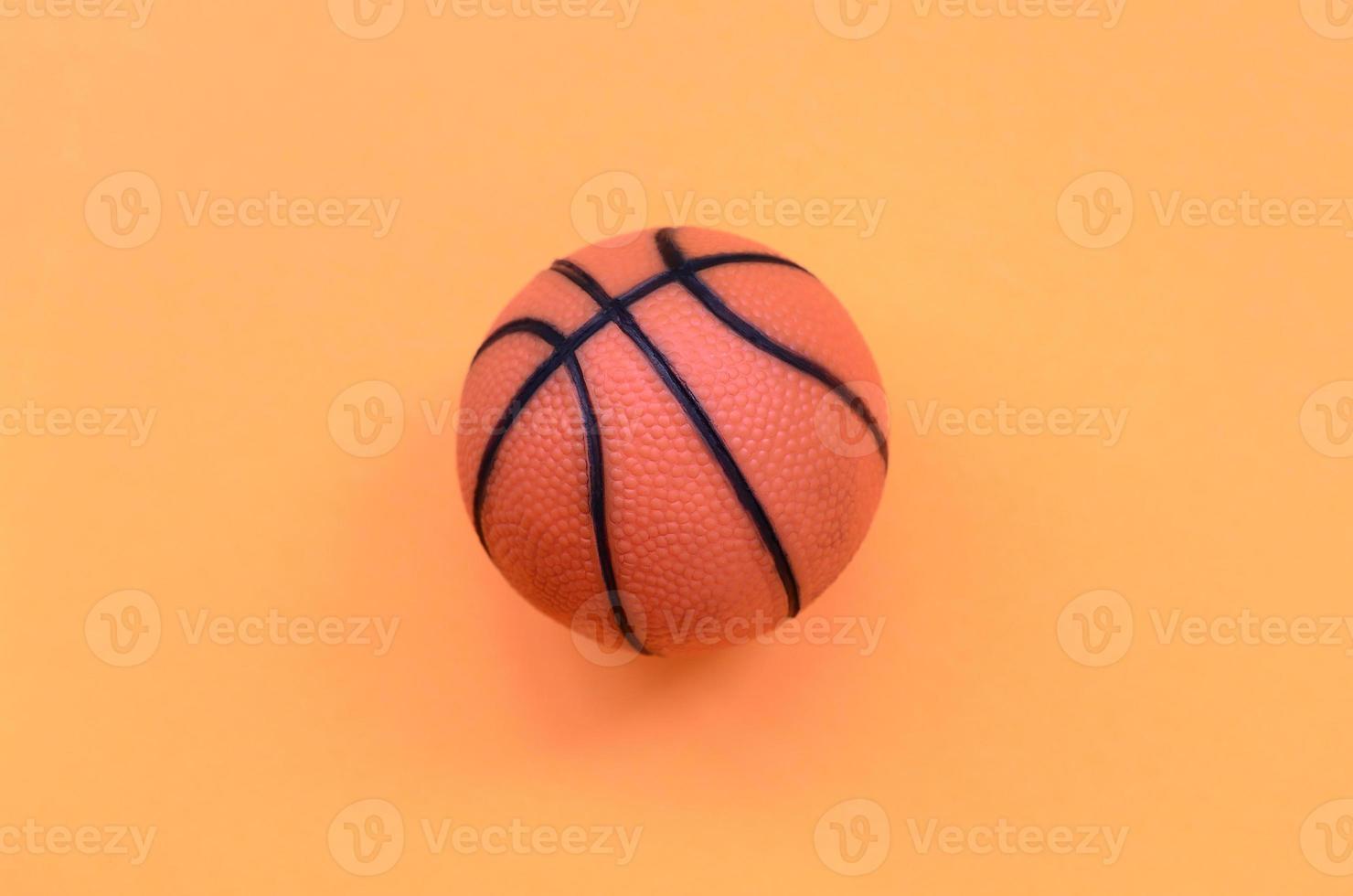 petite balle orange pour le jeu de sport de basket-ball se trouve sur fond de texture de papier de couleur orange pastel mode dans un concept minimal photo