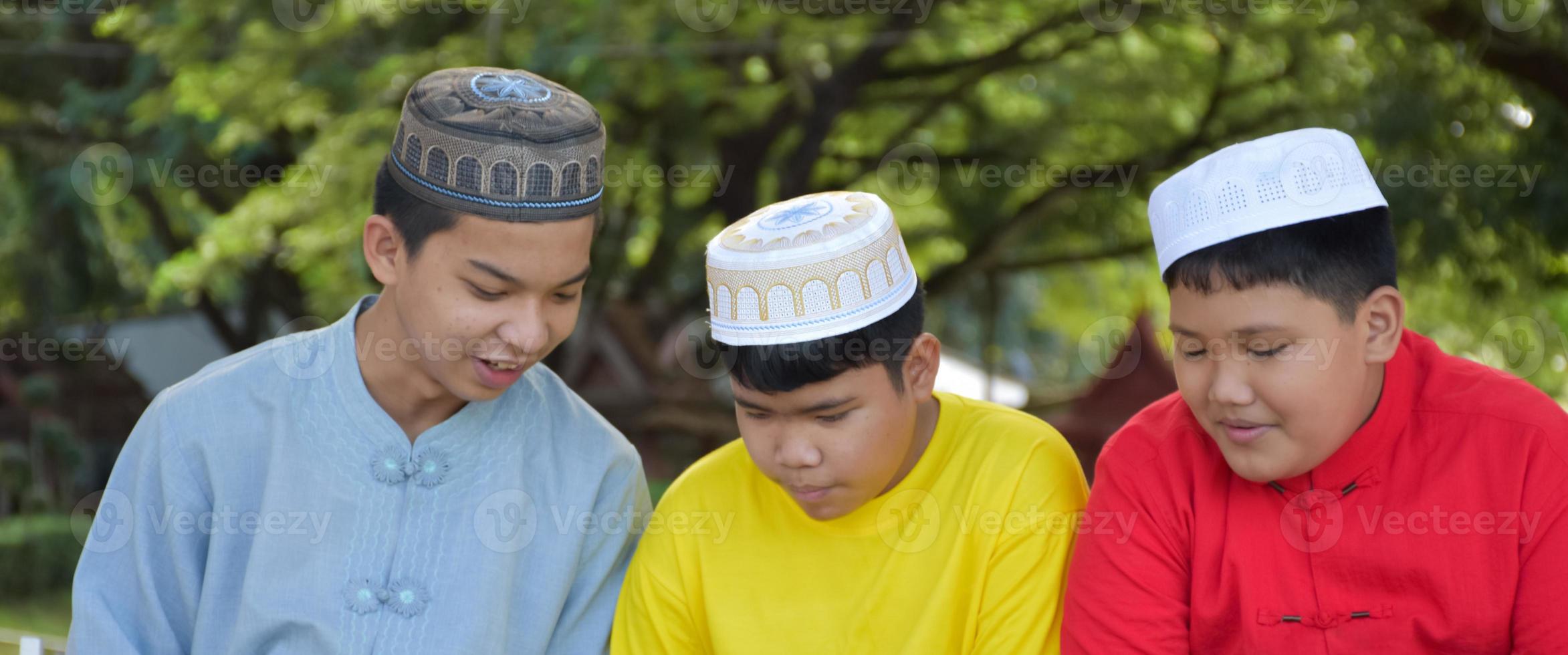 un groupe de garçons musulmans s'assoient ensemble sous l'arbre dans le parc de l'école, ils lisent, apprennent, parlent, suggèrent et consultent les problèmes d'apprentissage les uns aux autres, mise au point douce et sélective. photo