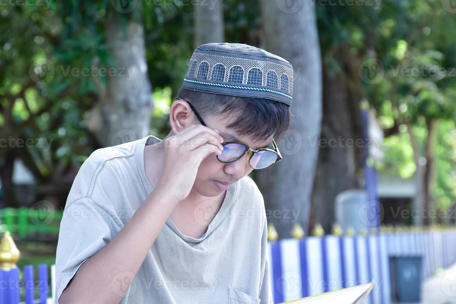 jeune garçon musulman asiatique porte des lunettes, assis dans le parc de l'école et lisant son livre pendant ses temps libres avant de rentrer à la maison, mise au point douce et sélective. photo