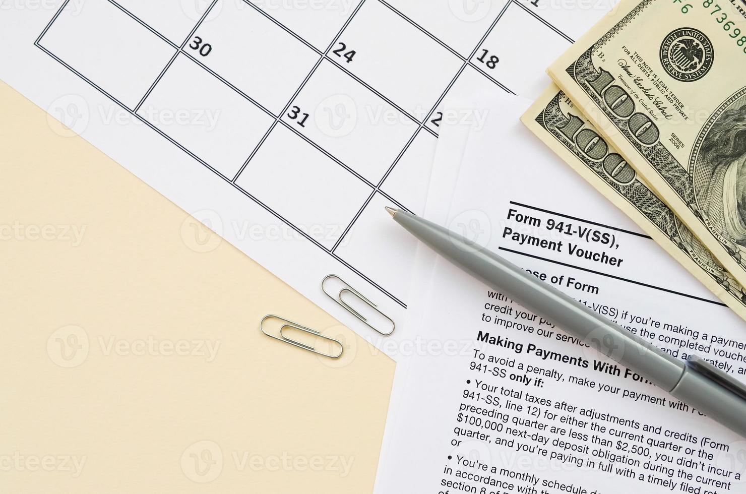 formulaire irs 941-v bon de paiement vide se trouve avec un stylo et de nombreux billets de cent dollars sur la page du calendrier photo