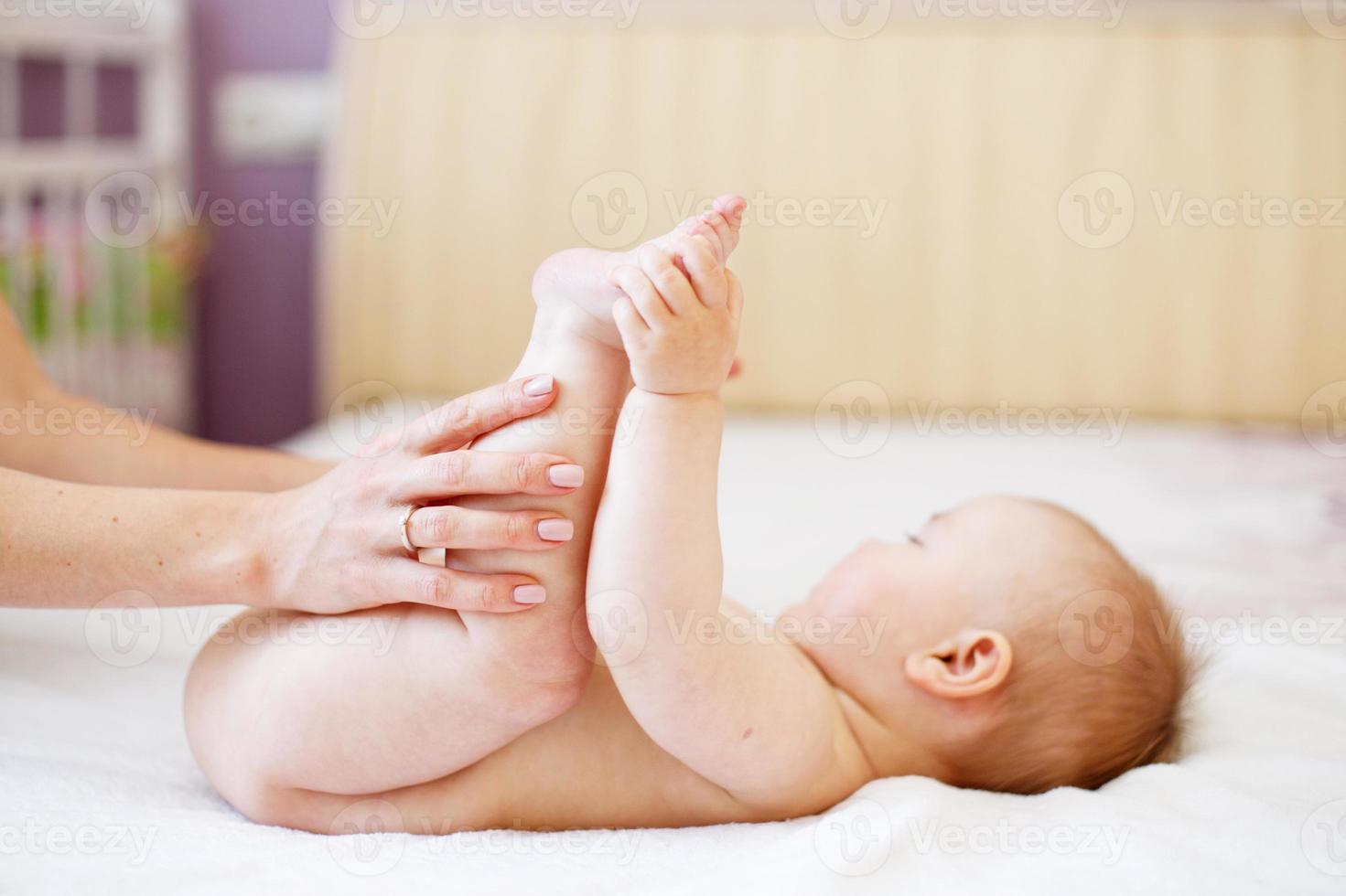 maman fait de la gymnastique pour un enfant. mère massant bébé au lit à la maison. photo